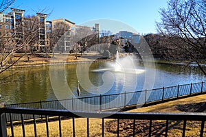A gorgeous shot of a silky green lake with a water fountain in the center of the water surrounded by yellow winter grass