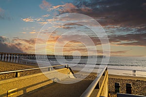 A gorgeous shot of a staircase and the vast blue ocean water and the pier at the beach with powerful clouds at sunset