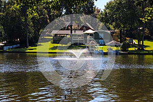 A gorgeous shot of the still blue waters of the lake with water fountain in the lake with lake front homes