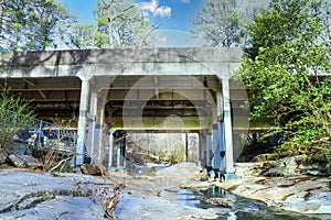 A gorgeous shot of a stone and metal bridge with a river running underneath with lush green and autumn colored trees on the banks