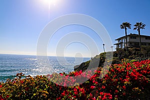 A gorgeous shot of the vast deep blue ocean water with waves rolling into the beach, homes on the cliffs with lush green palm tree