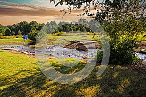 A gorgeous shot of a water running over the rocks in a creek in the park surrounded by lush green grass