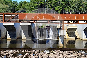 A gorgeous shot of the waterfall at Lake Peachtree with a rust colored iron bridge surrounded by rocks and lush green trees