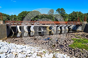 A gorgeous shot of the waterfall at Lake Peachtree with a rust colored iron bridge surrounded by rocks and lush green trees