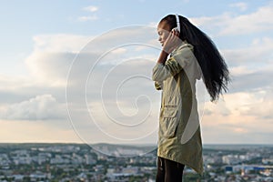 Gorgeous smiling african american girl listens music and relaxing. Blurred cityscape background. Outdoor portrait