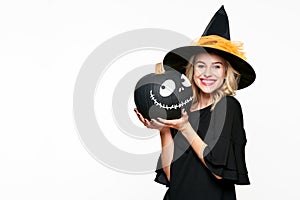 Gorgeous smiling Halloween Witch holding a Jack o Lantern. Beautiful young woman in witches hat and costume holding pumpkin.