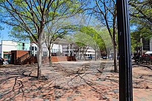 A gorgeous spring day in the Marietta Square with a red brick footpath surrounded by lush trees and black metal benches