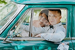 Gorgeous stylish blonde bride posing in retro green car with groom. The bride and groom are sitting inside the retro car