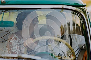 Gorgeous stylish blonde bride posing in retro green car with groom. The bride and groom are sitting inside the retro car