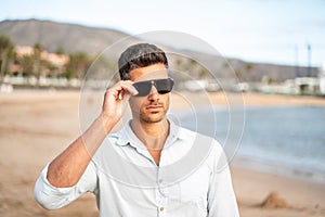 Gorgeous stylish man wearing fashionable shirt and sunglasses, walking on the beach