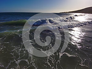 A gorgeous summer landscape at the beach with blue ocean water and water breaking into the shore at with blue sky at sunset