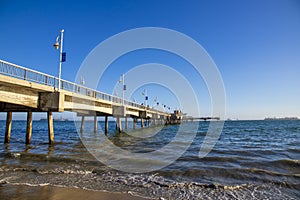 A gorgeous summer landscape at the Belmont Veterans Memorial Pier with blue ocean water and waves rolling into the beach