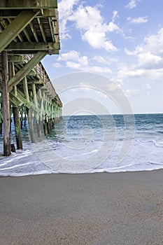 A gorgeous summer landscape at Crystal Pier with blue ocean water, brown sand, waves, blue sky and clouds in Wrightsville Beach