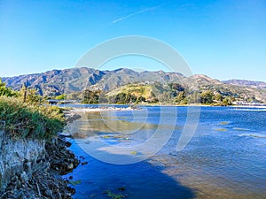 A gorgeous summer landscape at the Malibu Lagoon with deep blue lagoon water surrounded by lush green trees, grass and plants