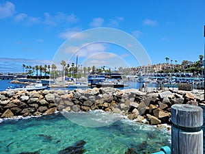A gorgeous summer landscape at Redondo Beach Pier with a jetty made of large rocks and boats and ships sailing in the harbor