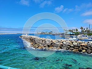 A gorgeous summer landscape at Redondo Beach Pier with a jetty made of large rocks and boats and ships sailing in the harbor