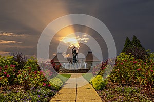 A gorgeous summer landscape with a water fountain with statue of a woman in the center surrounded by colorful flowers