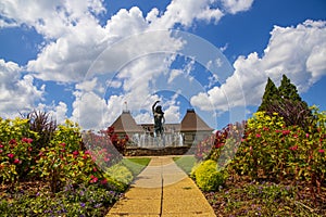 A gorgeous summer landscape with a water fountain with statue of a woman in the center surrounded by colorful flowers