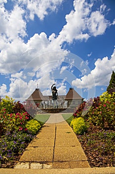 A gorgeous summer landscape with a water fountain with statue of a woman in the center surrounded by colorful flowers