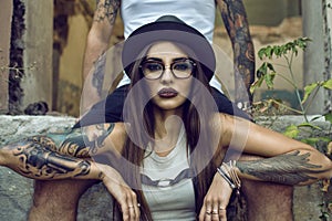 Gorgeous tattooed girl with provocative make up sitting between her boyfriend's legs in the ruined abandoned building