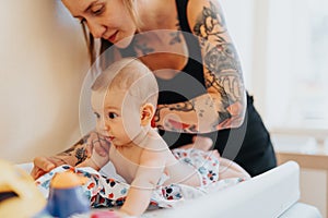 Gorgeous, tattooed mother changing her baby daughter diaper.
