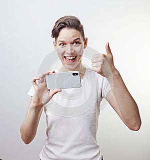 Gorgeous teenage girl is taking a photo using front camera in her smartphone and showing thumb up. Isolated on white background