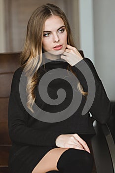 Gorgeous thoughtful woman in black dress sitting on leather sofa