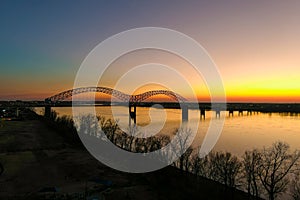 The gorgeous vast flowing water of the Mississippi river with a stunning blue, yellow and red sunset in the sky with a bridge over