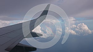 Gorgeous view at aircraft wing and rainbow between white clouds during flight