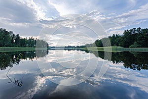 Gorgeous view of beautiful sky reflecting on a mirror of lake surface. Green forest trees bordering the lake on both size. photo