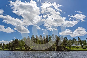 Gorgeous view of forest lake landscape on blue sky and white clouds background. Sweden.