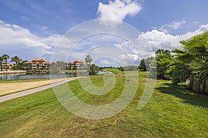 Gorgeous view of hotel building and blue water surface of pond and  green grass golf field on background blue sky with white cloud