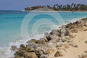 Gorgeous view of turquoise waves of Atlantic Ocean of rocky coast of island of Aruba against backdrop of sandy beach.