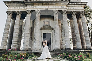 Gorgeous wedding couple embracing in sunlight near old castle in beautiful park. Stylish beautiful bride and groom gently hugging