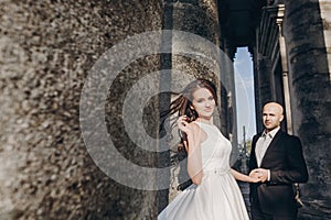 Gorgeous wedding couple embracing in sunlight near old castle in beautiful park. Stylish beautiful bride and groom gently hugging