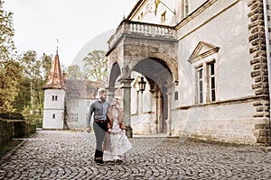 Gorgeous wedding couple hugging and walking near old castle in sunny beautiful park. Stylish beautiful bride and groom posing on