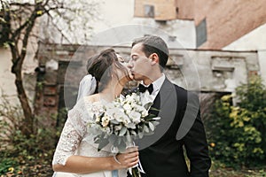 Gorgeous wedding couple kissing at old building. stylish bride with bouquet and  groom embracing  in european city street in