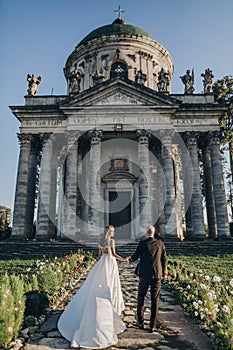 Gorgeous wedding couple walking near old castle in sunny beautiful park. Stylish beautiful bride and groom posing on background of