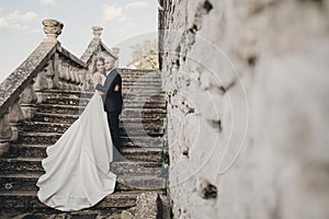 Gorgeous wedding couple walking on stone stairs near old castle in park. Stylish beautiful bride in amazing gown and  groom posing