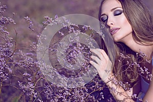 Gorgeous woman with artistic glam make up and long hair touching softly violet flowers with closed eyes enjoying their aroma photo