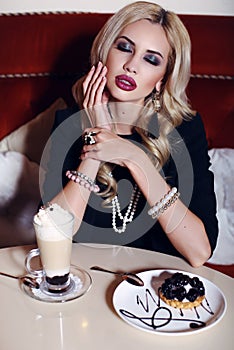Gorgeous woman with blond hair sitting in cafe with coffee and dessert