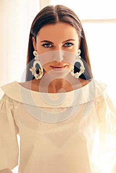 Gorgeous woman with dark hair in elegant clothes and fashion earrings posing with bouquet of yellow tulips