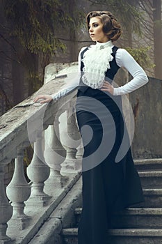 Gorgeous woman with elegant hairstyle wearing old-fashioned gown standing on old the steps on her castle