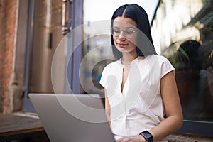 Gorgeous woman in fashionable glasses successful freelance worker connected to public wifi via laptop computer