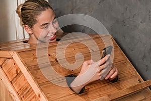 Gorgeous woman playing her mobile phone while using sauna cabinet.Tranquility