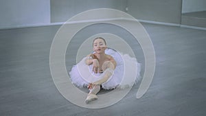 Gorgeous woman in white tutu dress in twine sitting on floor leaning lying down. Wide shot portrait of serious