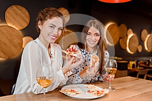 Gorgeous women smiling, posing and eating pizza in pizzeria.