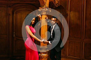 Gorgeous young african couple holding hands at the vintage column. Luxurious theatre interior background