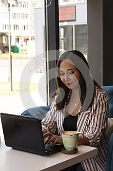 Gorgeous young business woman working remotely while sitting in front of an open laptop computer in the interior of a