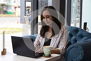 Gorgeous young business woman working remotely while sitting in front of an open laptop computer in the interior of a modern cafe